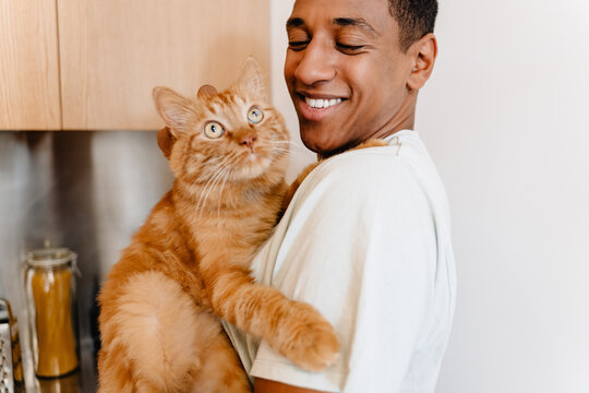 Black man wearing t-shirt smiling while petting his cat