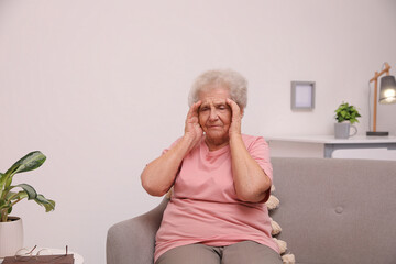 Senior woman with headache sitting on sofa at home