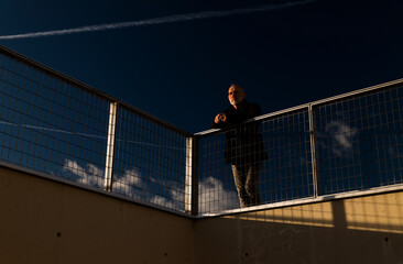 Adult man standing against fence with blue cloudy sky during sunset