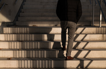 Rear view of adult man walking upstairs with sunlight and shadow