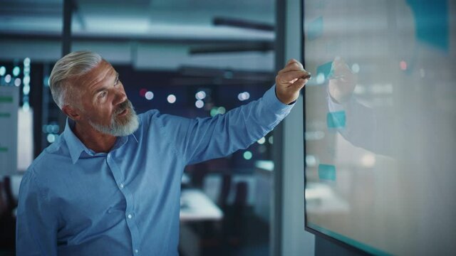 Company General Manager Holds Sales Meeting Presentation for Employees and Executives. Senior Adult Male Uses TV Screen with Growth Analysis, Charts, Ad Revenue. Work in Business Office.