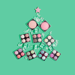 Creative Charistmas and New Year concept. Christmas tree made of makeup cosmetics and ice cubes on green background. Makeup artist Christmas greeting card.