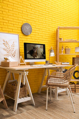 Stylish home office interior with comfortable workplace near yellow brick wall