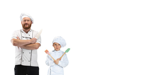 Young bearded man, cook, male chef in white uniform and his little assistant, child posing isolated on white background.