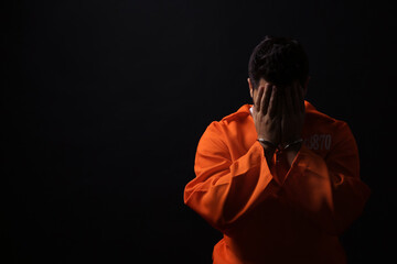 Prisoner in jumpsuit with handcuffs on black background, space for text