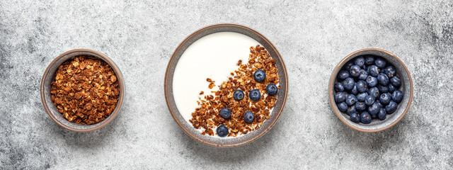 Granola with yogurt and blueberries in a line on a gray concrete background. Healthy healthy breakfast. Top view, flat lay. Banner.