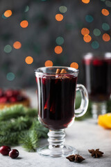  A glass of hot spicy mulled wine surrounded by spices and branches of a Christmas tree with bokeh in the background.