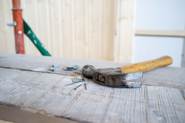 Hammer and nails lie on the scaffolding, against the background of a wall made of wooden slats. Work process. Home renovation.