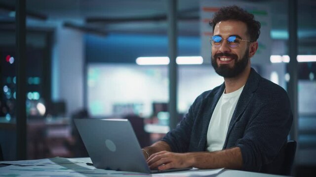 Modern Office Businessman or Manager Working on Computer, Smiling, Looking at Camera. Portrait of Successful IT Software Engineer in Glasses Working on a Laptop at his Desk.