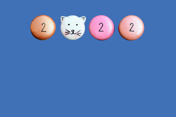 Three colorful round macaroons with numbers and one in the shape of cat on a blue background, isolated. Original greeting card for the new year 2022, copy space for text 