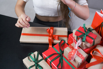 woman tying ribbon with red string to gift wrap covered with kraft paper on black table, for...