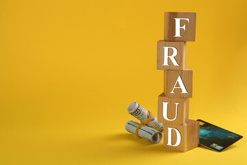 Wooden cubes with word Fraud, credit card and money on yellow background, space for text