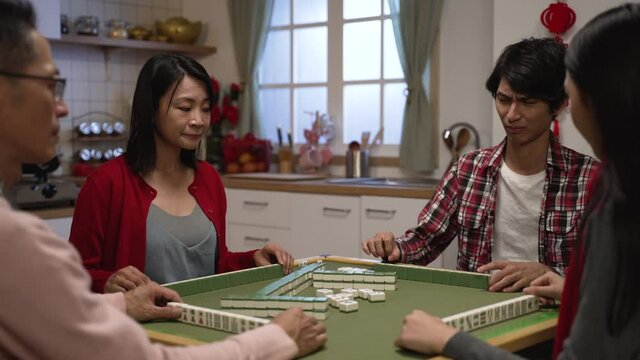 mother clothing making eye gesture to her son for the wanted tile while they are cheating together in mahjong game at home on chinese lunar new year's eve