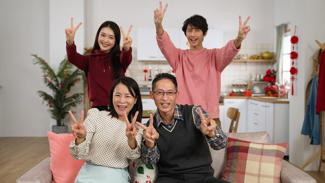 happy family of four smiling at camera with thumb and victory hand gestures while taking burst photos in a modern house interior with chinese lunar new year decorations