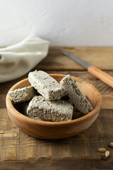 Sunflower halva in a wooden bowl with an old knife and a psalm on a wooden table. Rustic style. Traditional sweets. Vegetarian food. Copy space. Vertical orientation.