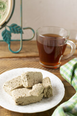 Several pieces of sunflower halva on a white saucer with a cup of tea on a wooden table in the kitchen. Rustic style. Traditional natural sweets. Vetikal orientation.