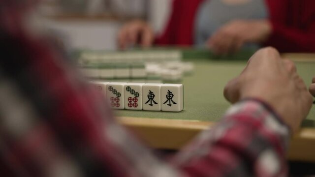 closeup with selective focus of mahjong pieces and a player's hand tapping on table. waiting for his turn. classic asian strategy tile game concept. chinese text translation: east