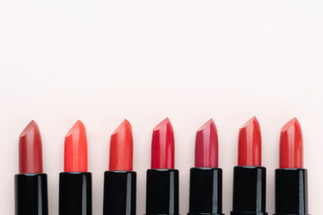 Red lipsticks of different shades on beige background. Makeup and cosmetics concept. Close up. Flat...