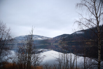 View of the Norwegian lake river in cloudy rainy weather through the trees. Norway in November. Resting place near the river lake. Mountain view in Norway.