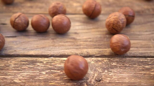 Macadamia nuts in shells fall on the old wooden vintage board. Slow motion.