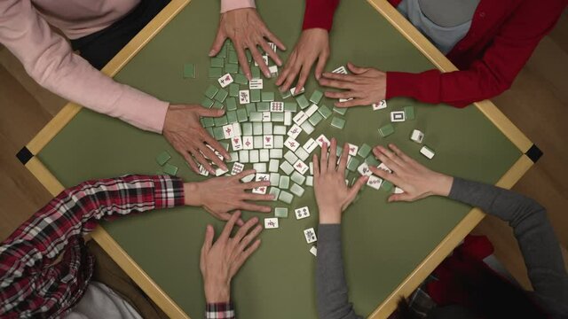 top angle shot with cropped view of family's hands mixing the face-down mahjong pieces on green table while playing tile game on chinese lunar new year's eve at home