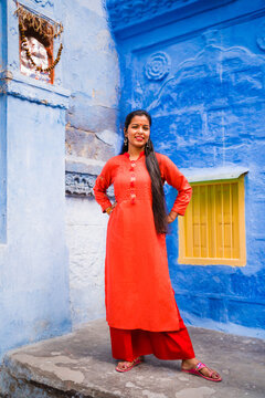 Beautiful Indian female model at blue district of the old city in Jodhpur, Rajasthan, India. Hindu girl with long hair, tilak and traditional Indian red kurta next to a Ganesh statue. 
