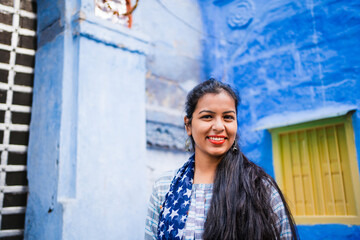 Beautiful Indian female model at blue district Chandpole of the old city in Jodhpur, Rajasthan, India. Attractive girl with long hair in modern clothes, blue jeans and blue background. 
