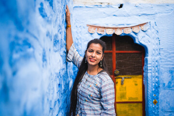 Beautiful Indian female model at blue district Chandpole of the old city in Jodhpur, Rajasthan, India. Attractive girl with long hair in modern clothes, blue jeans and blue background. 