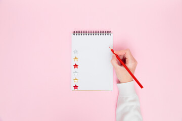 Female hand writing in white blank open spiral notebook with stars isolated on pastel pink background. Flat lay, copy space. Creative work, business, to do list or education concept.