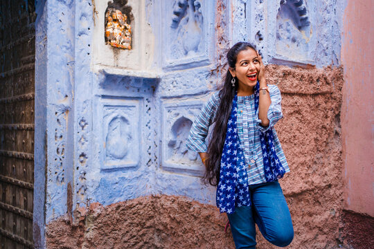 Beautiful Indian female model at blue district Chandpole of the old city in Jodhpur, Rajasthan, India. Attractive girl with long hair in modern clothes, blue jeans and blue background. 