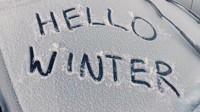 words hello winter written by hand on glass of a car covered by snow