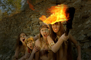 Four girls are dressed as Neanderthal warriors. Their 
faces are filled with anger and are seen waving a 
blazing torch in a stone quarry