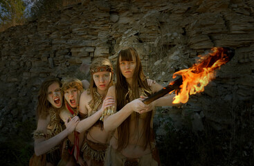 Four girls are dressed as Neanderthal warriors. Their 
faces are filled with anger and are seen waving a 
blazing torch in a stone quarry