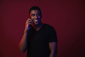 Young black man in t-shirt smiling while talking on cellphone