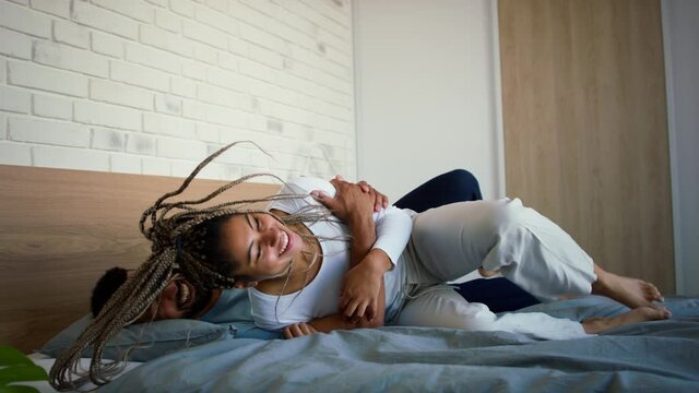 Happy multiracial young couple in love laughing and having fun on bed indoors at home.