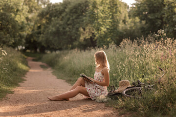 a girl in a sundress with a hat and a bicycle reads a book