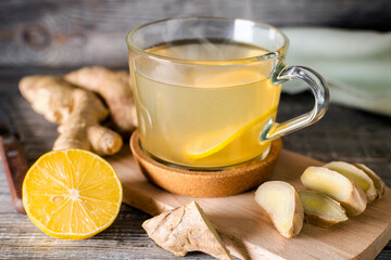 Glass cup of hot ginger tea with lemon slice on a wooden cutting board. Natural organic antiflu...