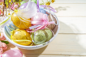 Easter painted colorful pastel eggs in a basket, with feathers on a light wood background. Easter greeting card composition, spring holiday still life background