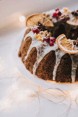 Traditional Christmas fruit cake decorated with glaze, orange, cranberries and nuts on the table