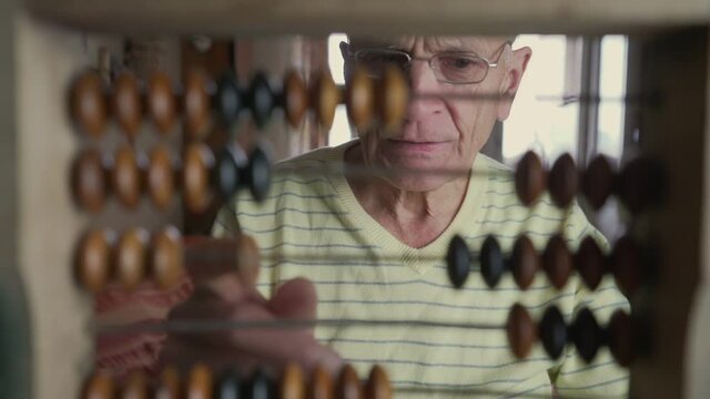 Elderly male person in glasses calculating with vintage wooden abacus. Bookkeeping and home accounts department concept.