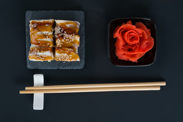 on a black table, top view, rolls with eel, ginger, laid out in the form of a rose and wooden sticks