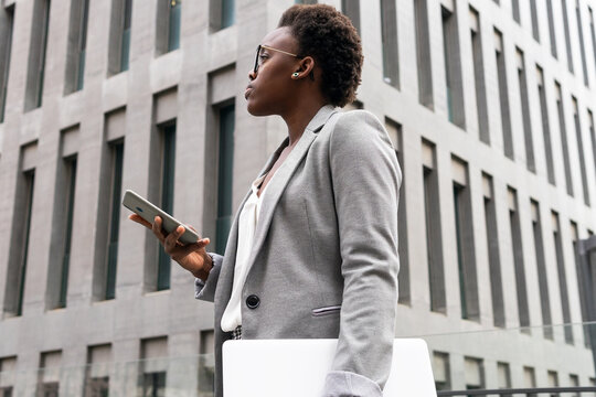 Black female entrepreneur with laptop ans mobile phone in street near office building
