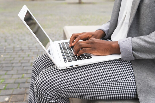 Crop black woman checking email on laptop sitting in street