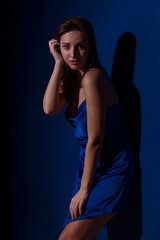 Young and cute brunette woman in blu dress posing on dark blue background free space for text