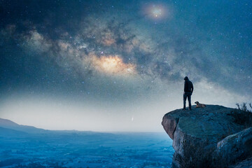 man standing on the top of the mountain, back view, with his dog and  Milky Way over the valley 
