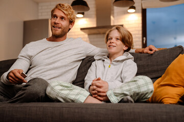 Ginger son and father watching TV while sitting on sofa together