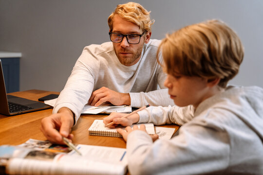 Ginger son doing homework with his father while sitting at desk