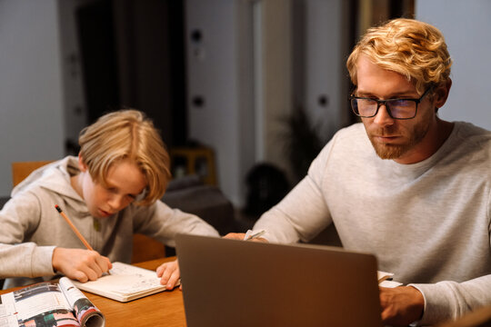 Ginger son doing homework while his father working with laptop