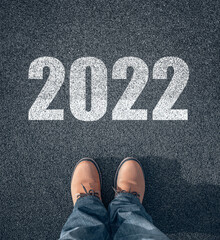 New year 2022, concept. 2022 inscription on the asphalt. The man in boots takes a step into the new year 2022.