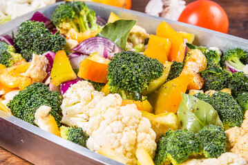 Cooking vegetable stew - chopped cauliflower, broccoli, tomatoes, onions and bell peppers in a baking sheet, close-up